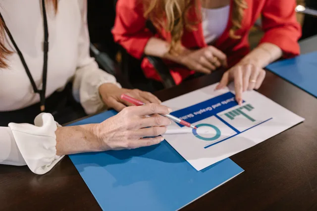 Two women analyzing business charts and reports during a meeting at a wooden table. Reading operations case studies metrics without fooling yourself